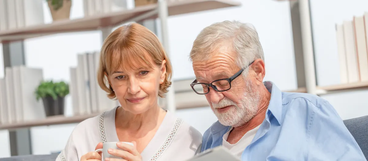 An older couple sitting together on a sofa reading a document.